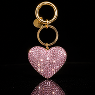 Pink crystal heart keychain and purse charm with polished gold-tone hardware on a black reflective background.