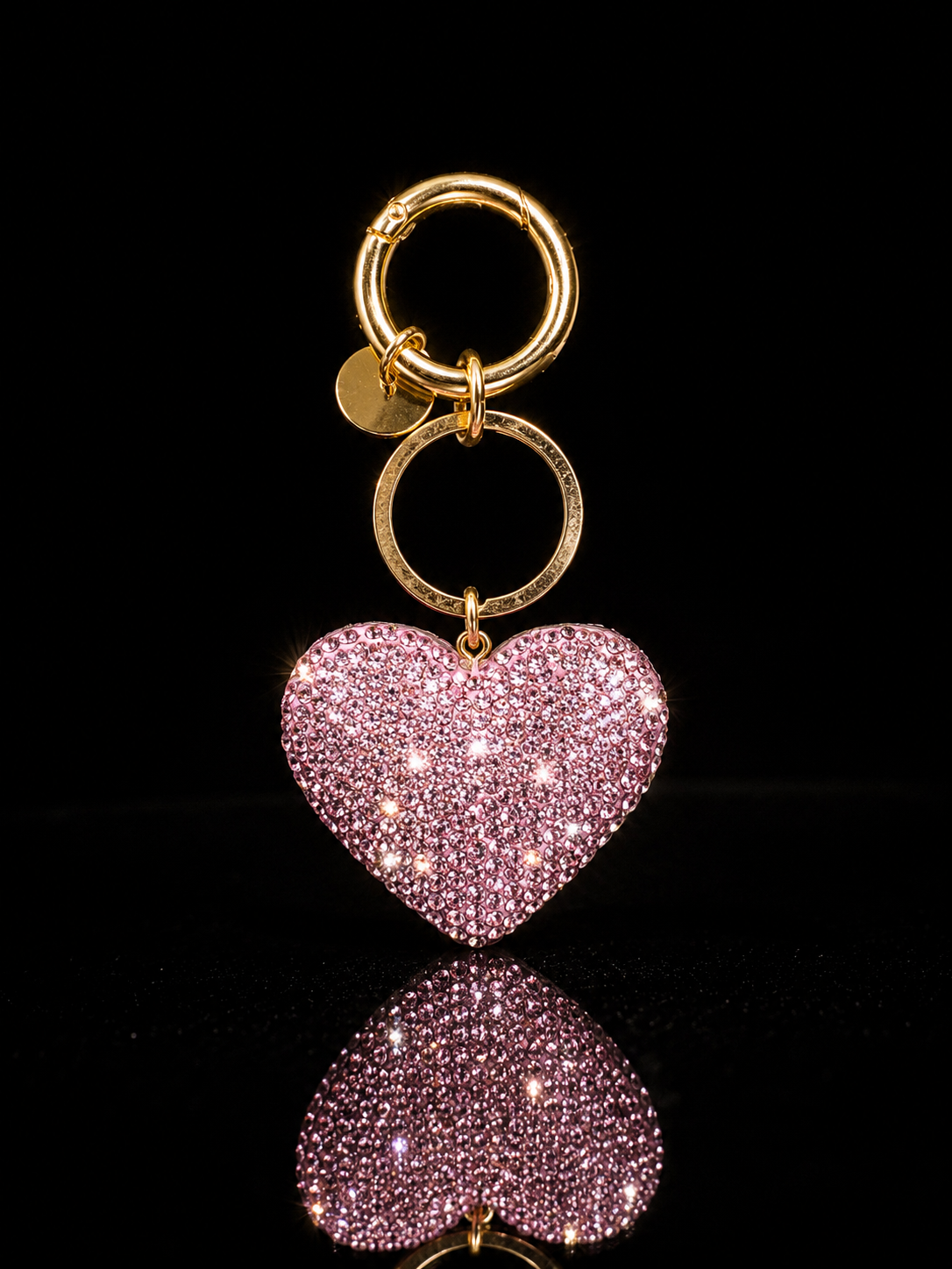 Pink crystal heart keychain and purse charm with polished gold-tone hardware on a black reflective background.
