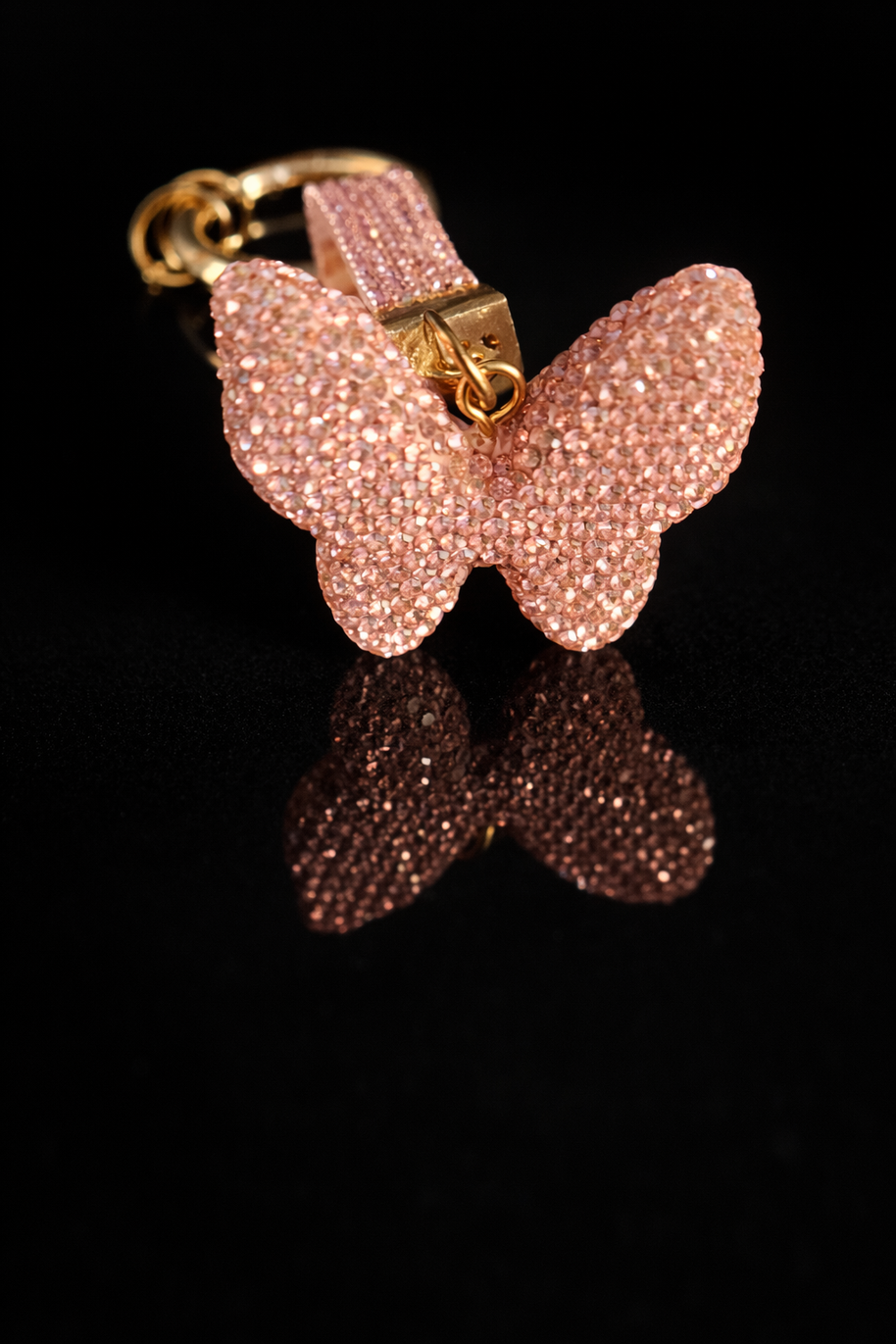 Pink crystal butterfly keychain and purse charm with polished gold-tone hardware on a black reflective background.