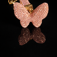 Pink crystal butterfly keychain and purse charm with polished gold-tone hardware on a black reflective background.