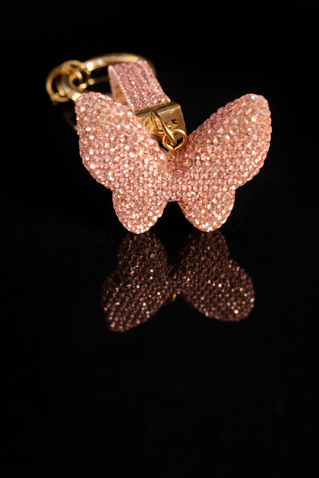 Pink crystal butterfly keychain and purse charm with polished gold-tone hardware on a black reflective background.