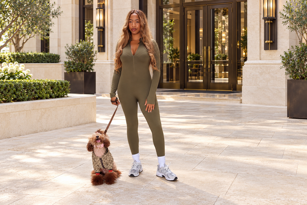 Woman in an olive jumpsuit with her smiling poodle outside a hotel entrance.