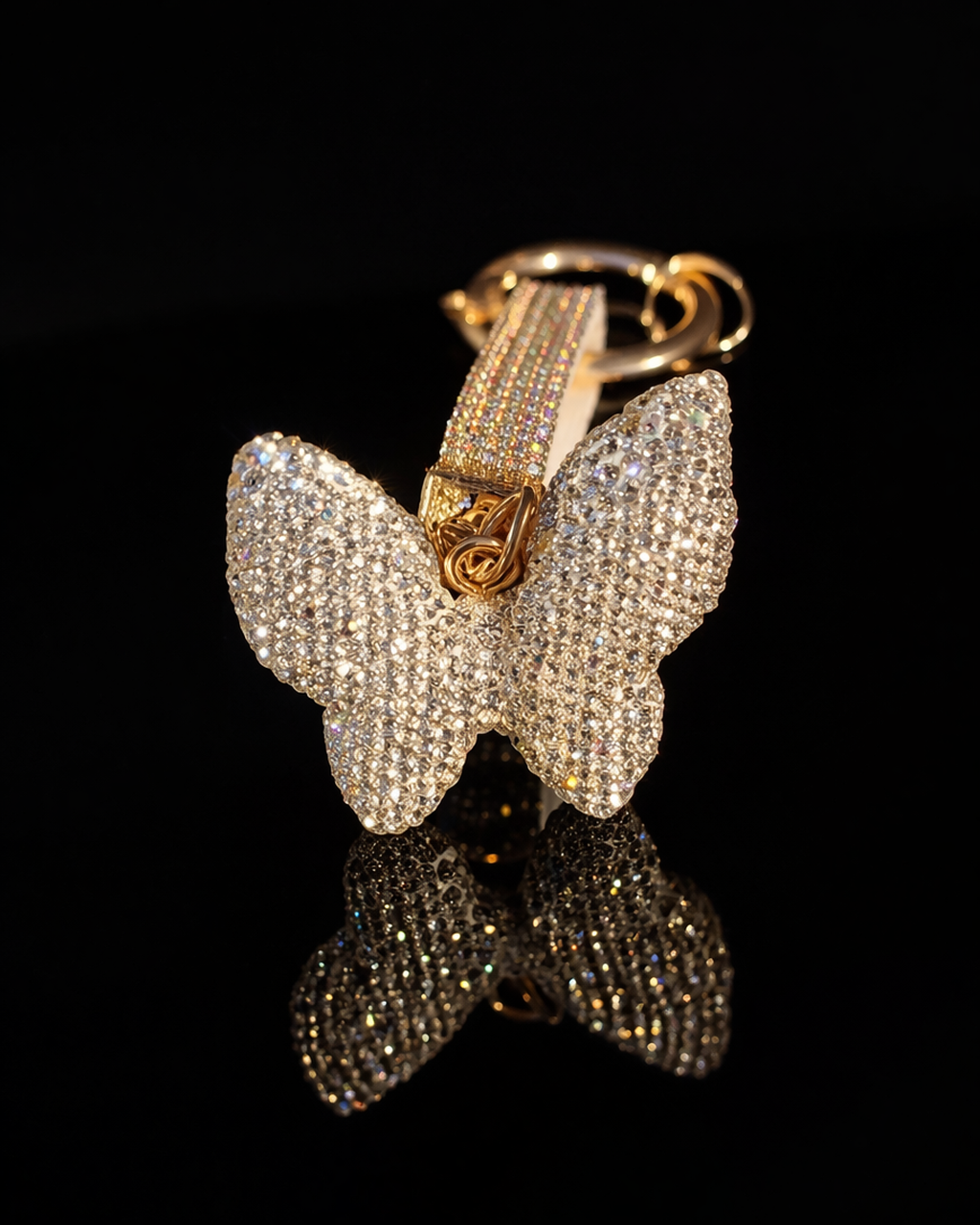 Crystal butterfly keychain and purse charm with polished gold-tone hardware on a black reflective background.